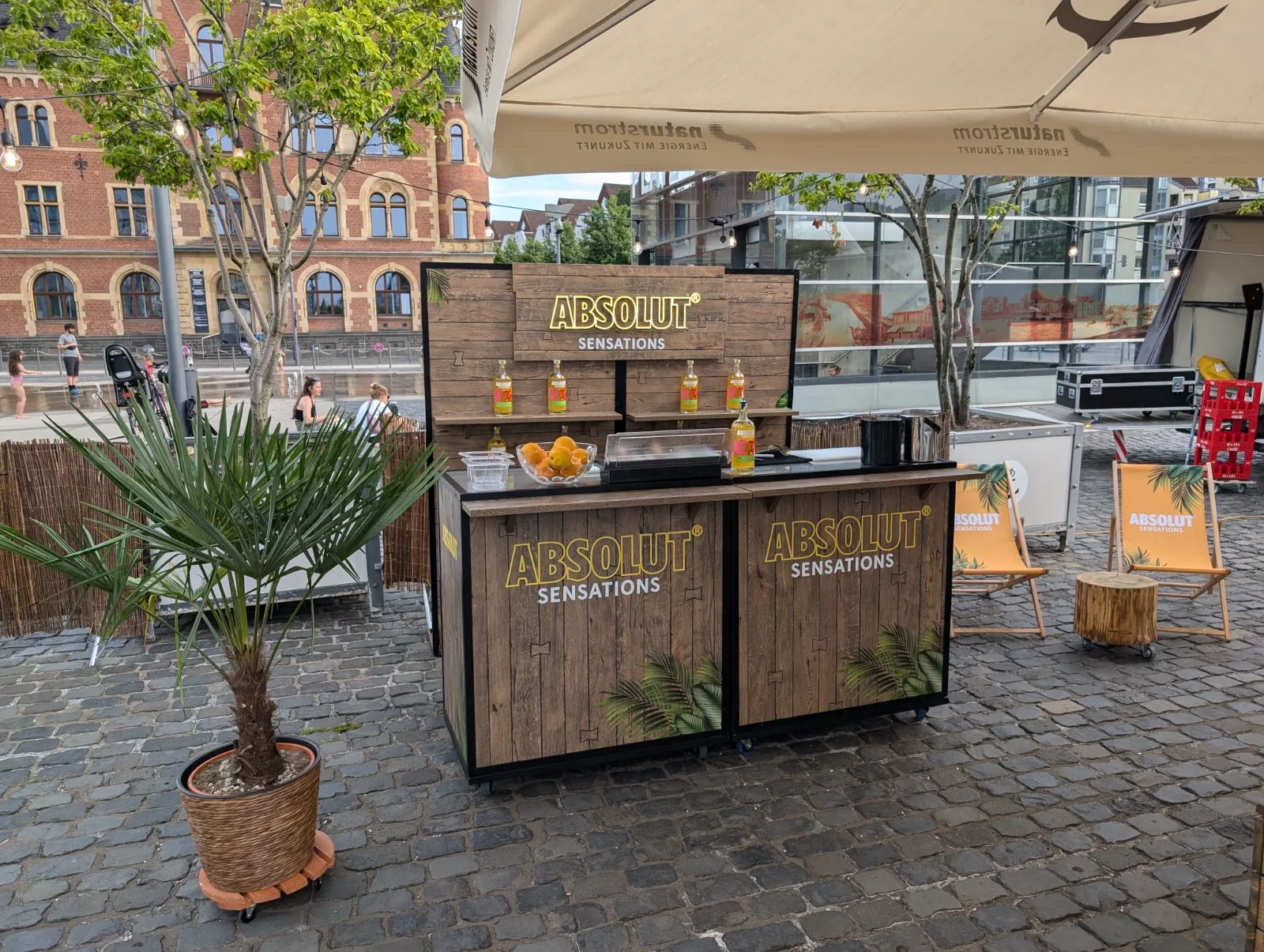 Mobile Absolut-Sensations-Bar mit Sonnenschirm und Liegestühlen auf einem Platz in der Stadt