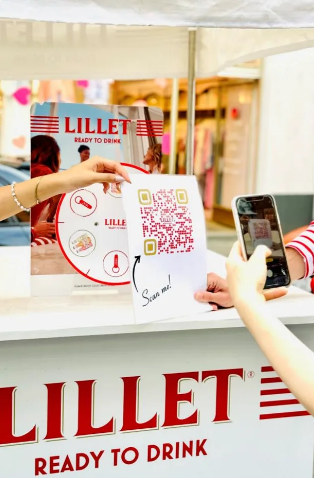Lillet-Sampling-Stand mit QR-Code, den eine Passantin mit dem Smartphone scannt