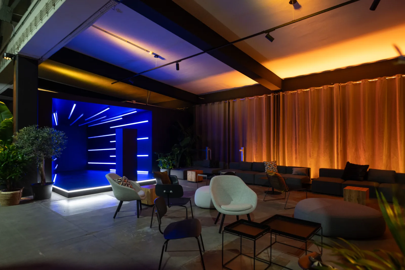 Lounge-Bereich mit warmem Vorhanglicht und blau beleuchteter Bühne im Hintergrund