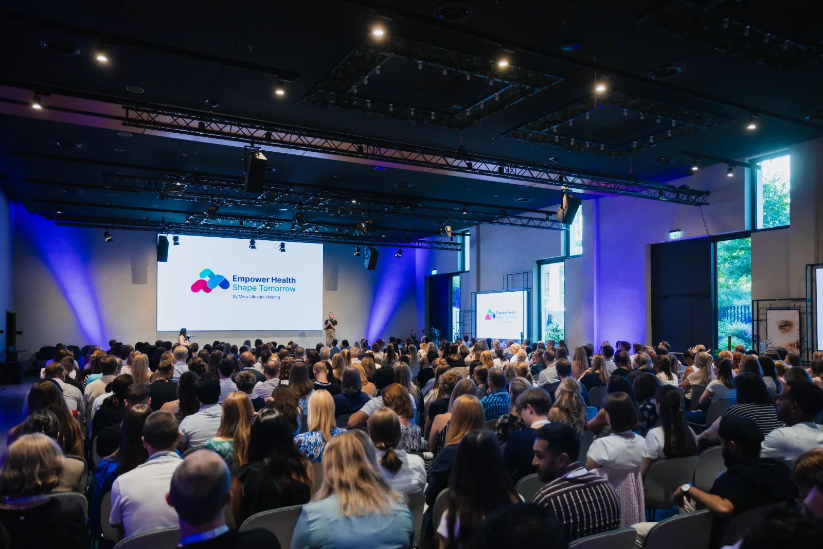 Voller Saal beim Merz Lifecare Summit in Frankfurt, auf der Bühne das Motto Empower Health Shape Tomorrow